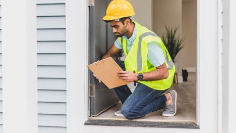Home inspector checking a doorway while holding a clipboard during a property condition review.