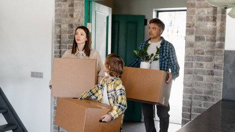 Family carrying moving boxes into a new home, representing a VA buyer closing successfully.