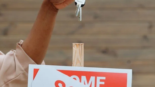 Hand holding house keys above a Sold sign after a real estate transaction.