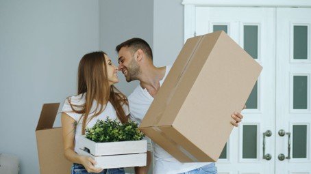 Couple carrying moving boxes into a new home, representing buying before selling in Mansfield, Texas.