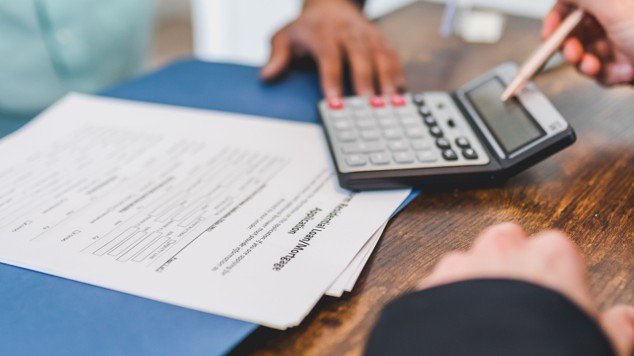 Hands using a calculator on real estate documents to estimate a property tax bill.