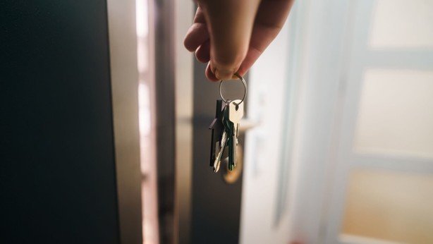 Hand holding house keys inside a doorway for a Dallas-Fort Worth first-time home buyer program blog.
