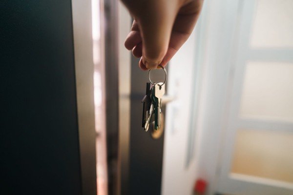 Hand holding house keys in a doorway for a Texas first-time home buyer program qualification article.