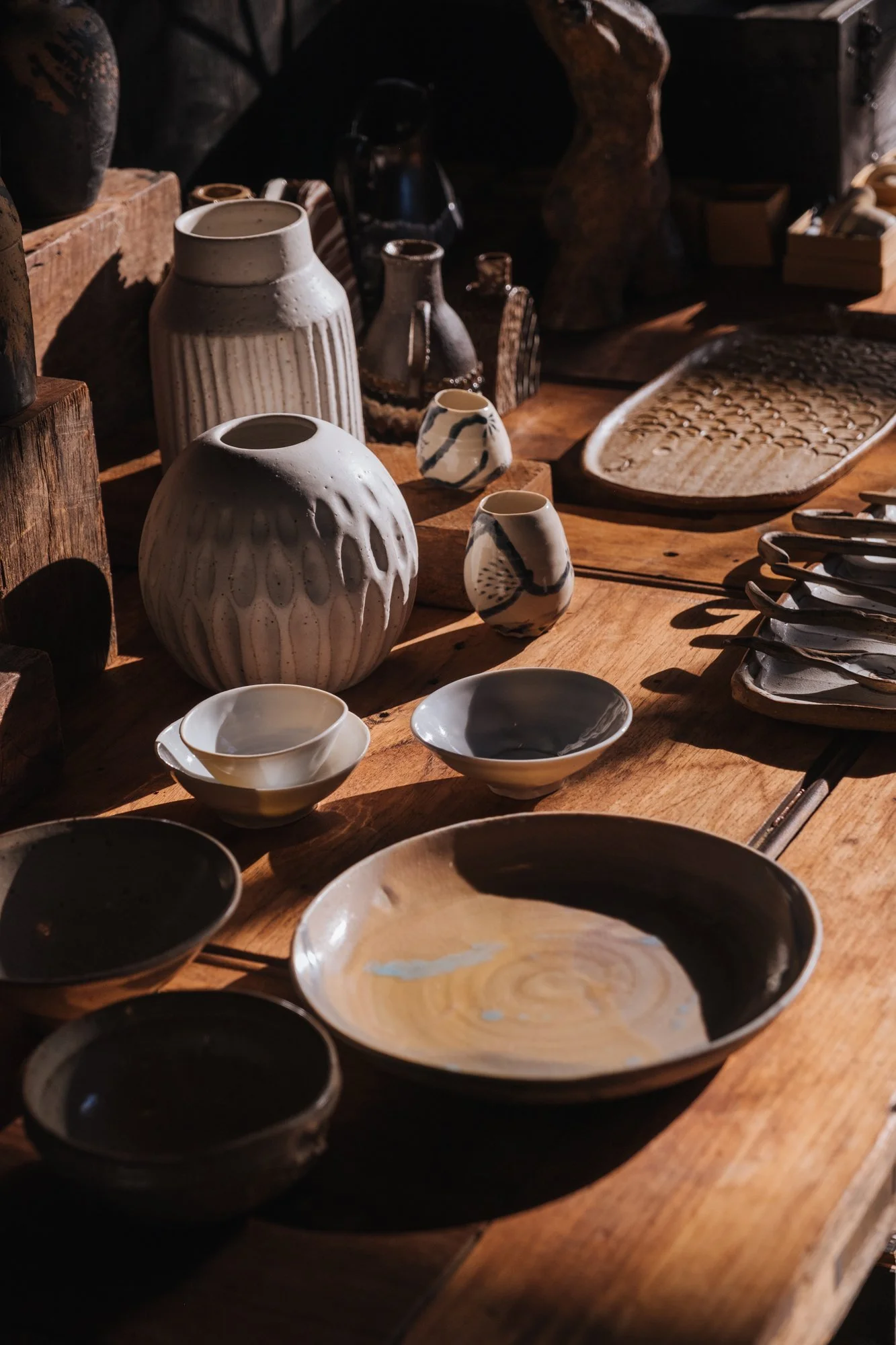 A close up of earthen colourd handmade ceramics on a timber table in the afternoon light