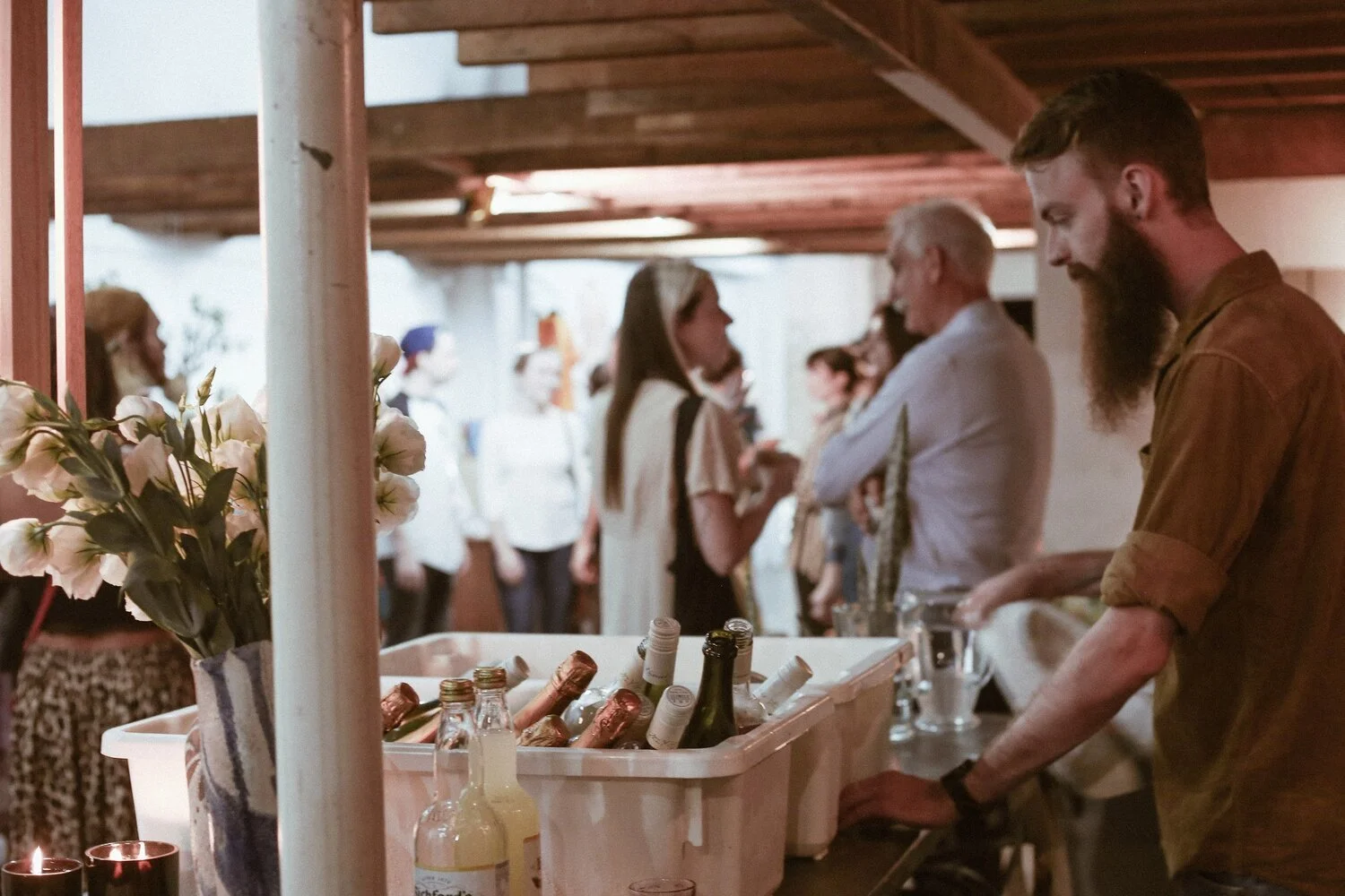 View of Vacant Assembly bar and bottles of wine/champagne in focus.  Background is out of focus and there are people chatting to each other