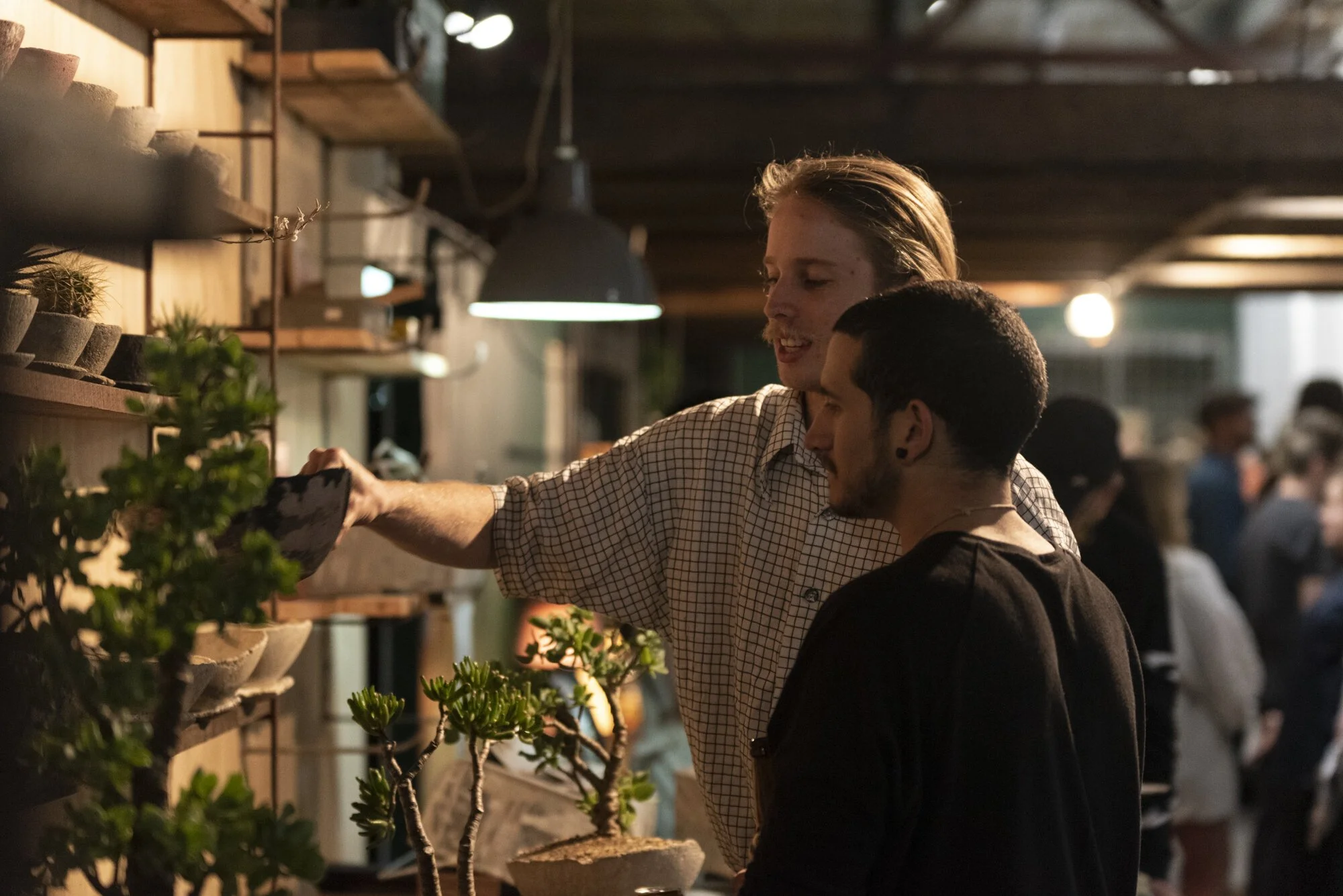 Two men are looking at a display ofhandmade industrial concrete pots at Vacant Assembly. One of them has picked up a black medium sized pot.