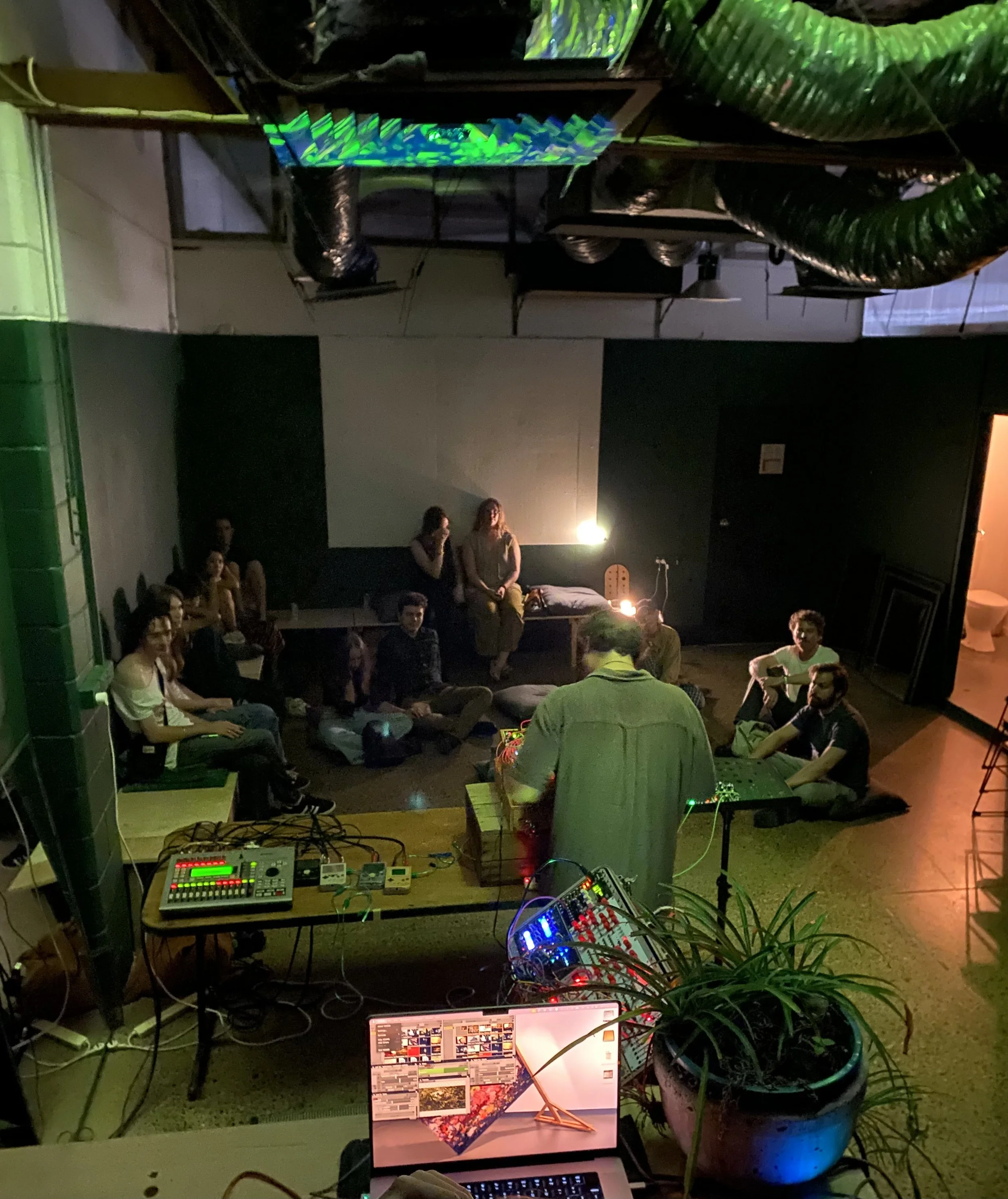 People in the foreground around big circular platters of food.  In the background are people milling around at a Vacant Assembly event.