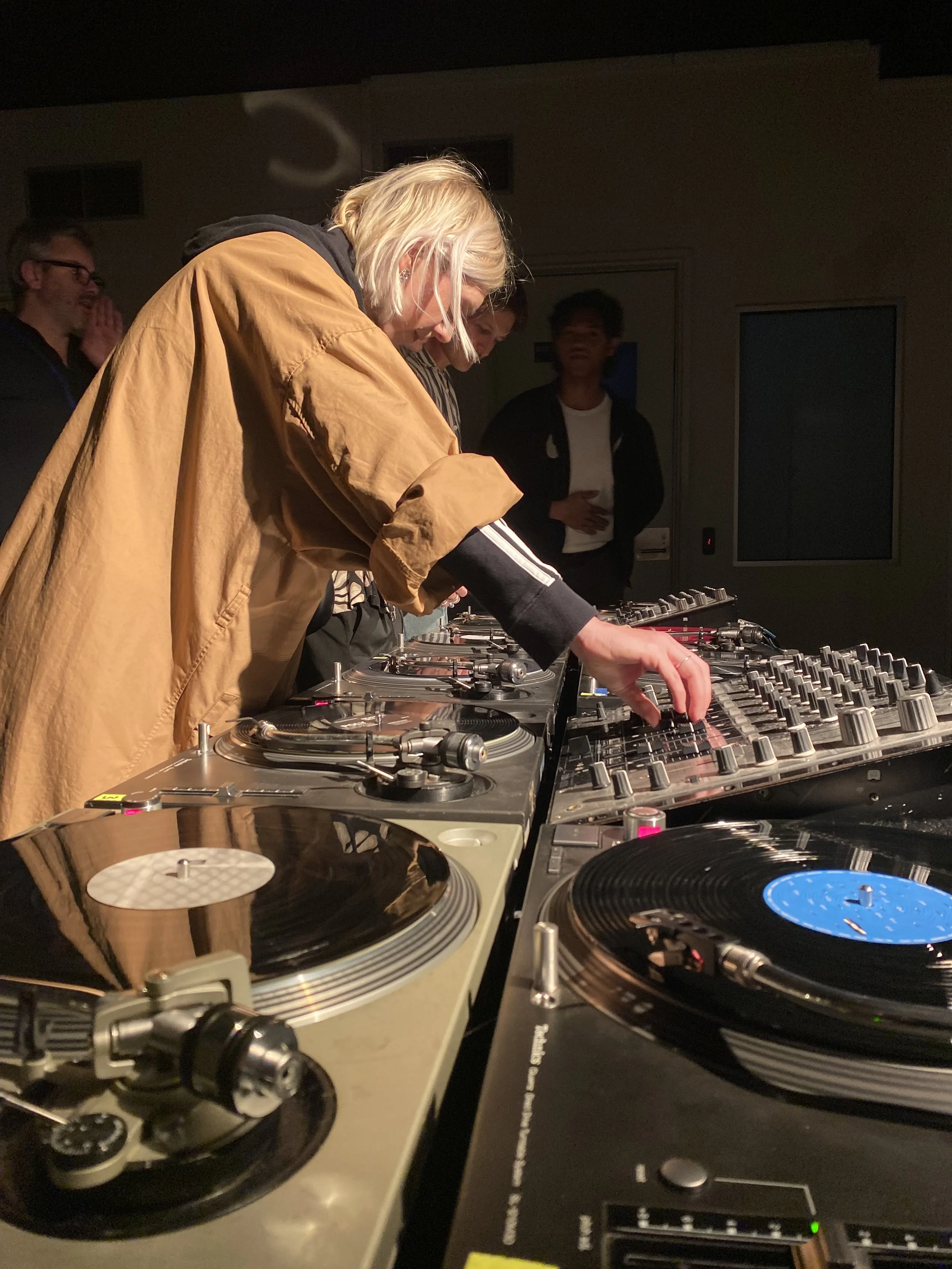 A woman is modelling in front of a white block wall in Vacant Assembly.  There is a photographer and videographer in the foreground building content