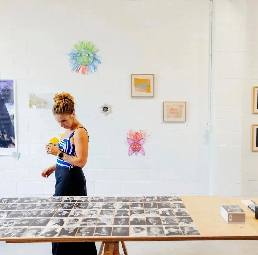 A women looking at a table of black and white photographs in a group exhibition at Vacant Assembly