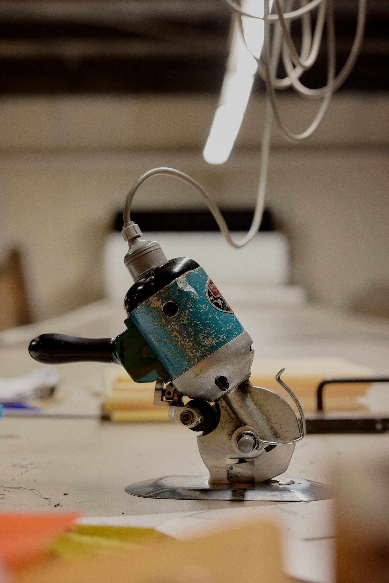 A small vintage handheld electric paper hole puncher with a black handle, attached to a power cord, resting on a desk or table surrounded by papers and scattered debris.