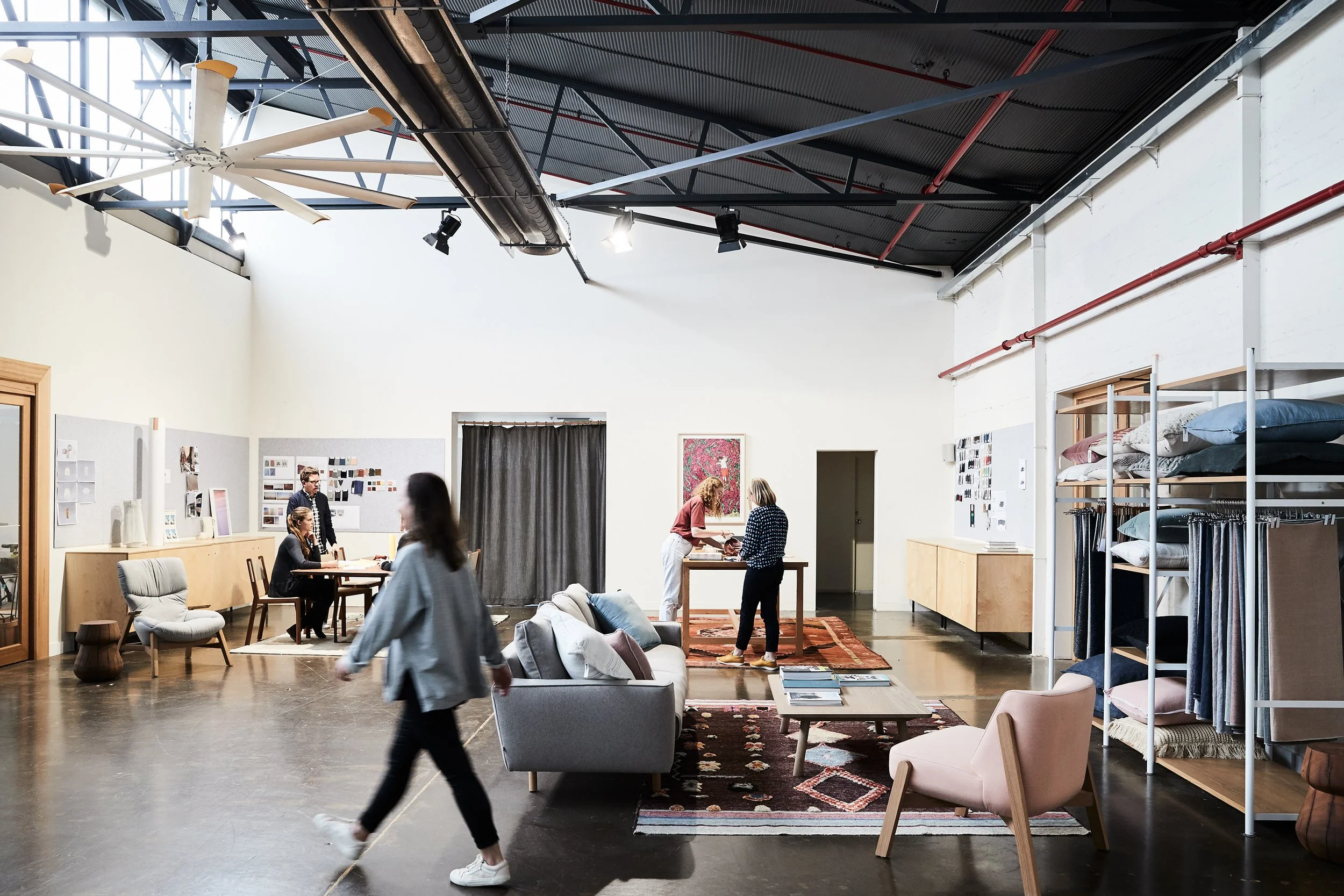 Interior of a modern furniture store with sofas, chairs, and display shelves, with people shopping and browsing.
