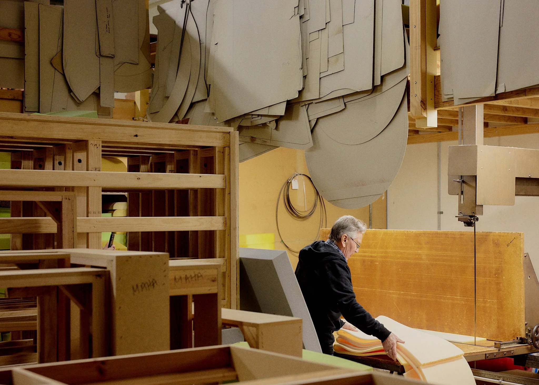 A person working in a woodworking or craft workshop, surrounded by large sheets of material, wooden frames, and equipment.