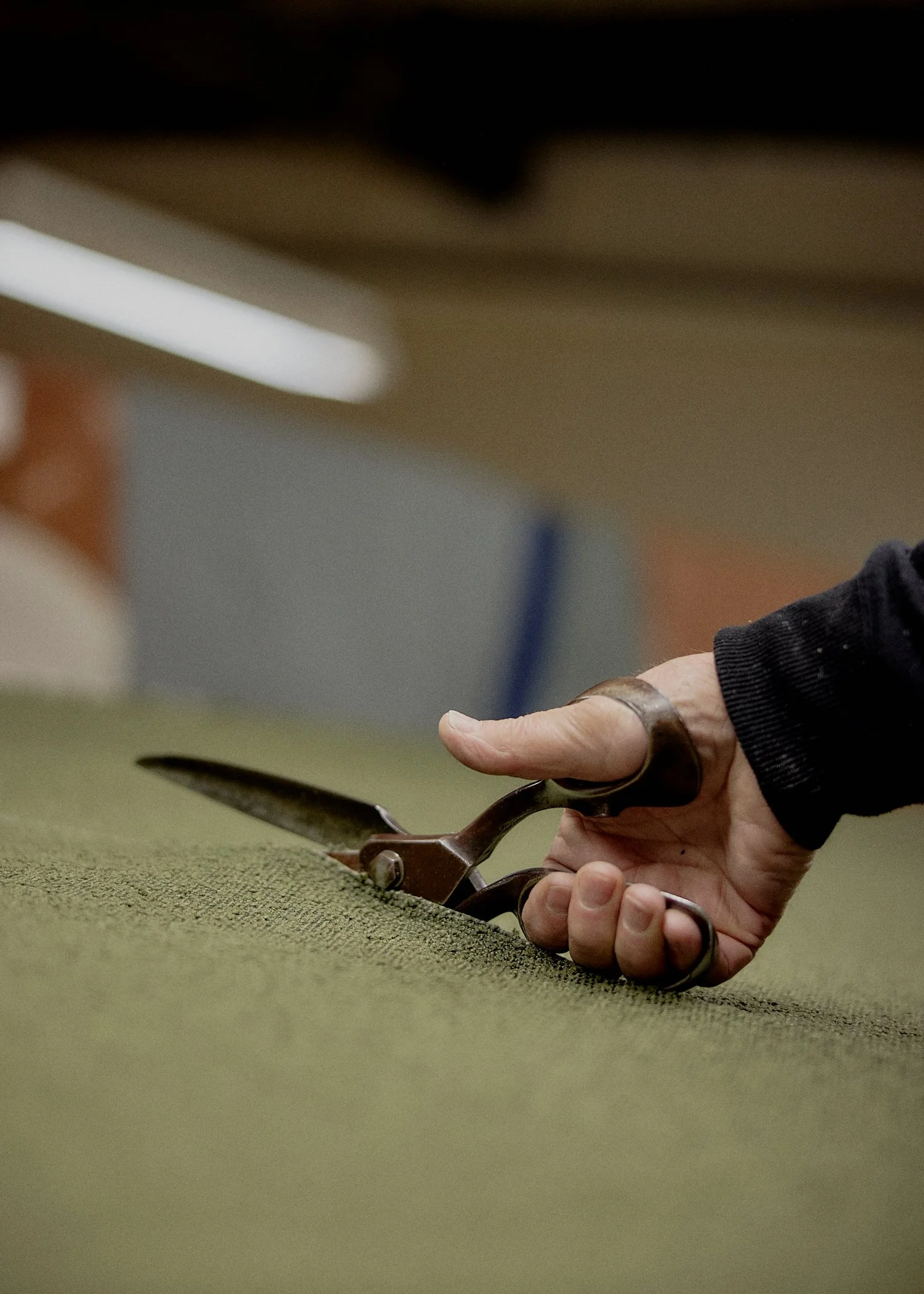 A person's hand holding a pair of scissors, cutting through a piece of fabric or material.