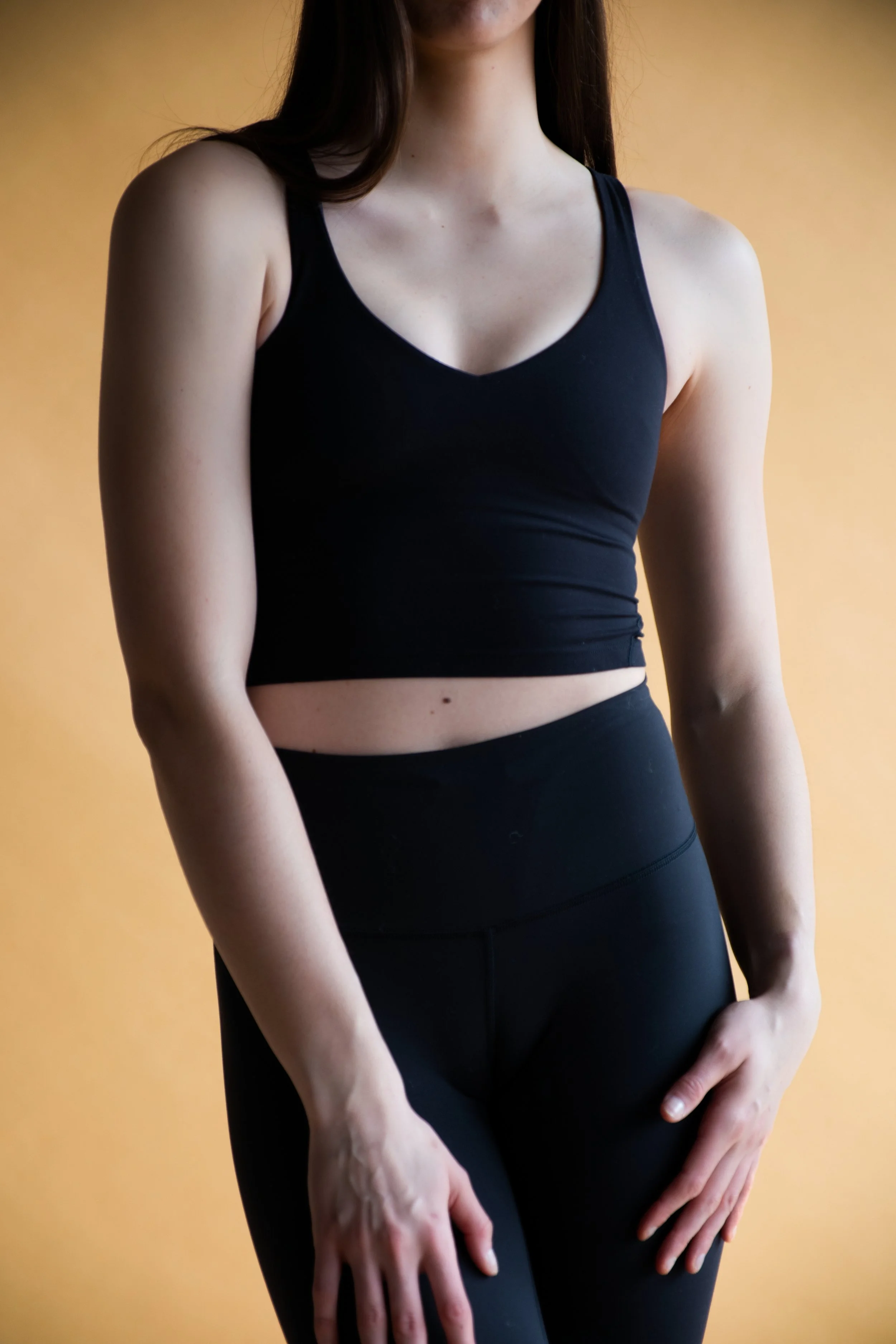 A woman in a black athletic tank top and matching leggings standing against a yellow background.