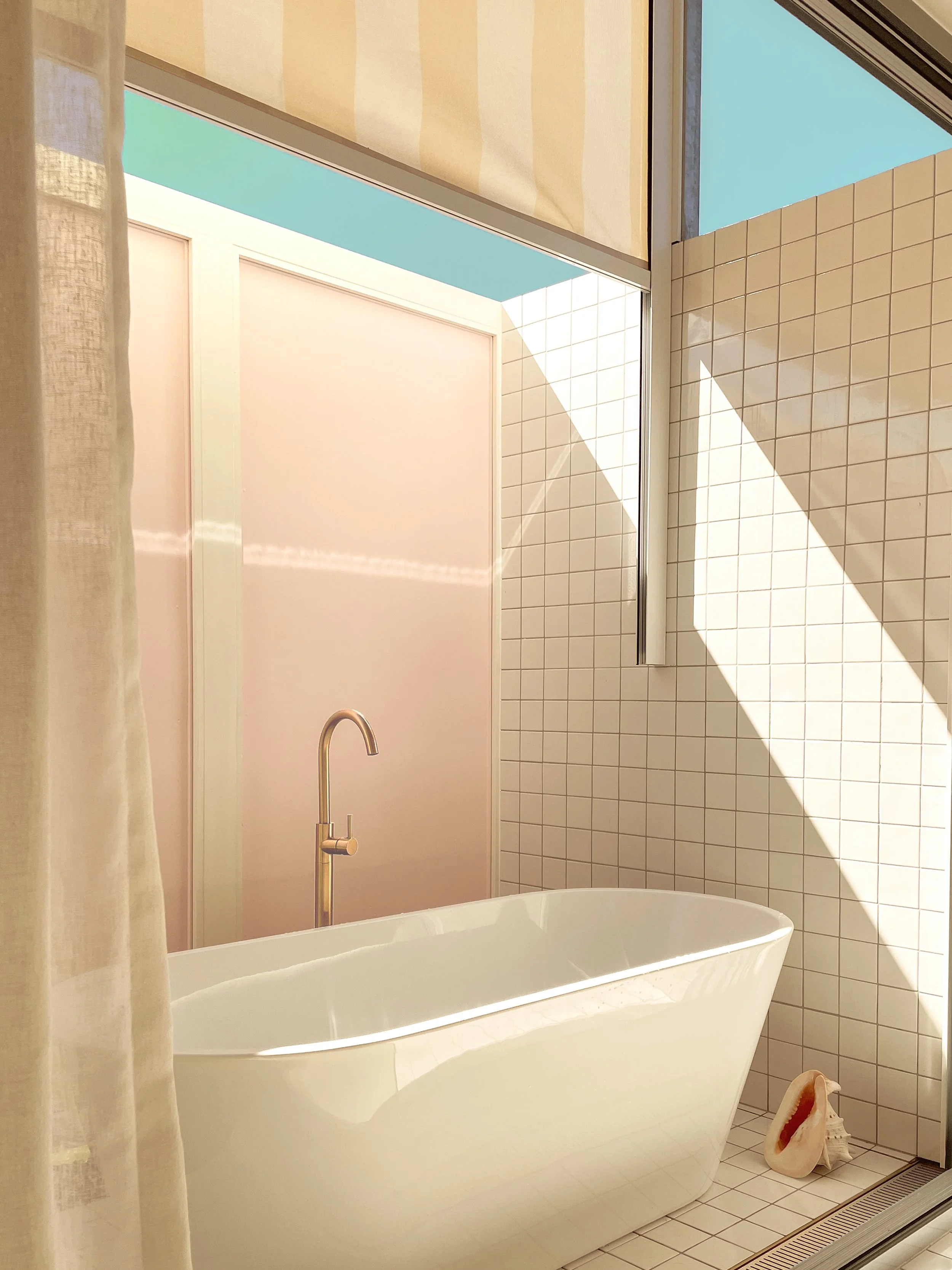 Sunlit bathroom at Daydream House with freestanding bath, soft pink walls and tiled surfaces