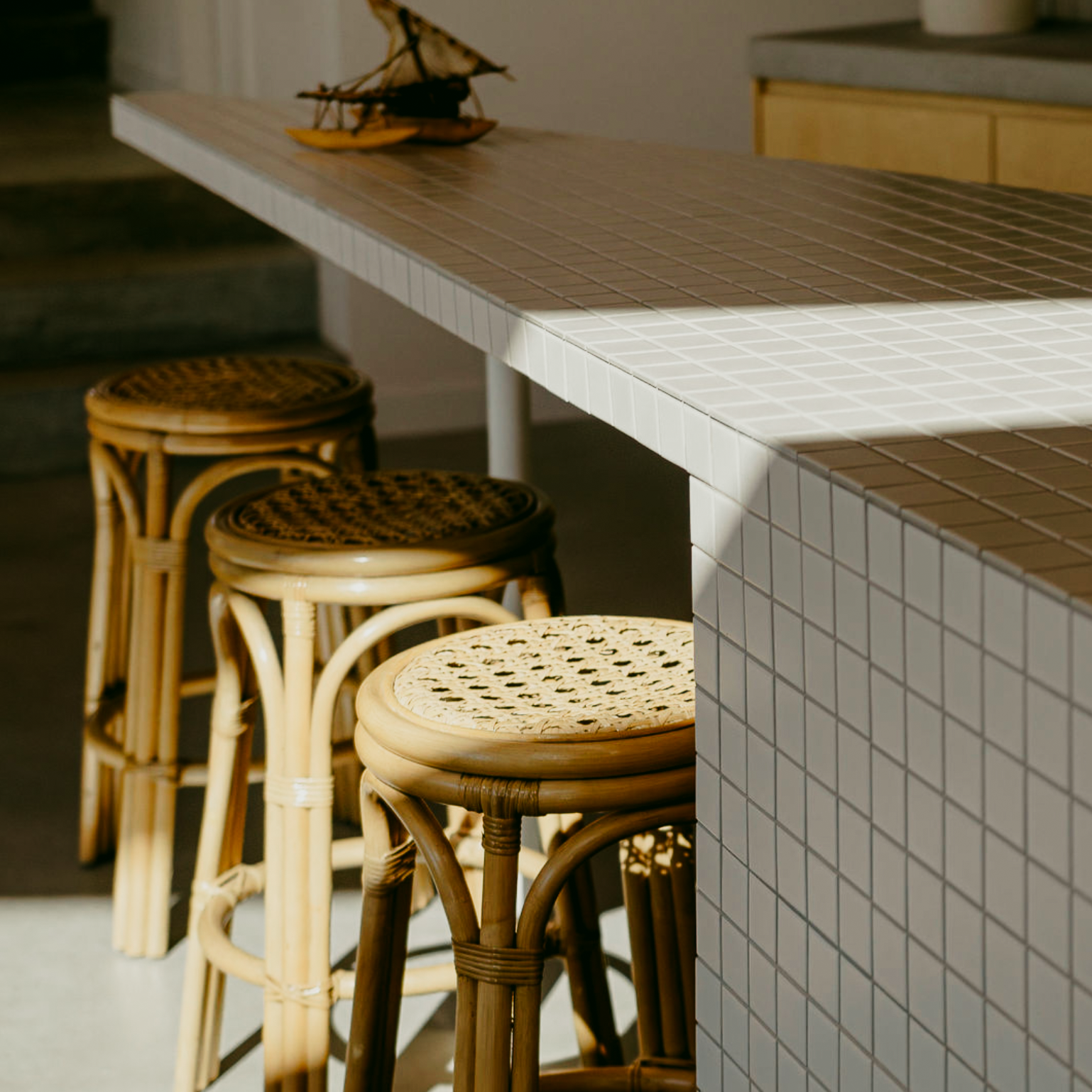 Interior detail of the Daydream House showing tiled kitchen island bench, rattan stools and warm natural light