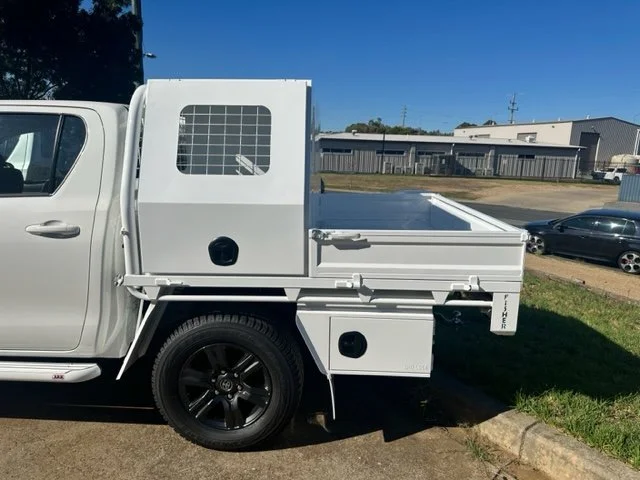 White ute with a flatbed and a small enclosed compartment in the back, custom fabricated ute tray flatbed. Powder coated and sandblasted, and installed. Custom designed and welded ute tray.