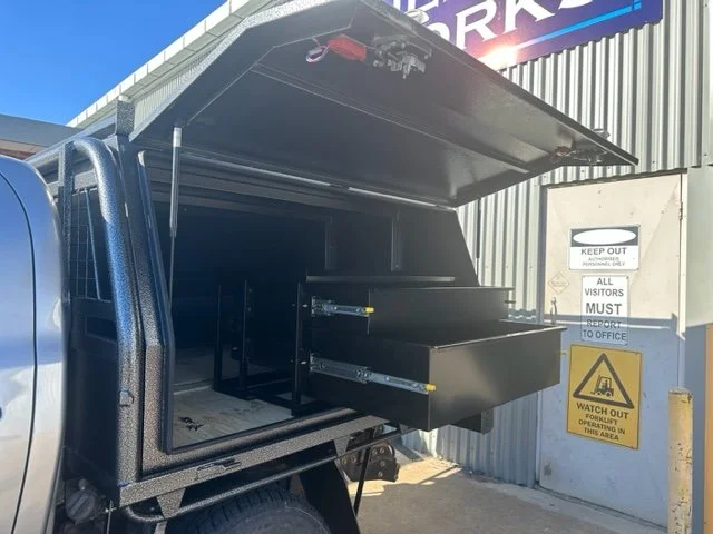 Black mobile storage unit inside a vehicle with an open side hatch, custom fabricated ute tray flatbed. Powder coated and sandblasted, and installed. Custom designed and welded ute trays in Wagga Wagga