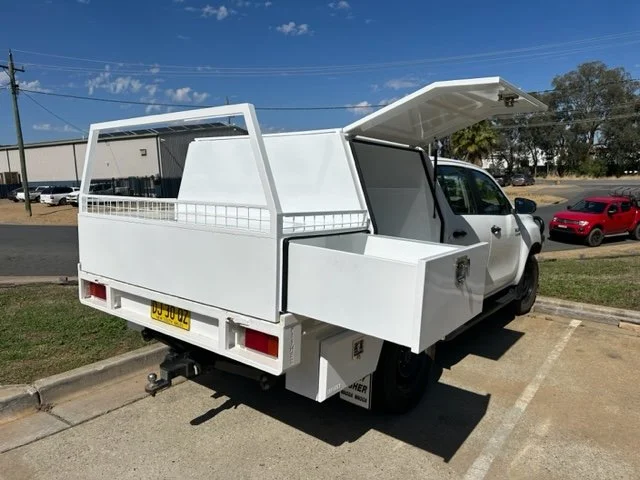 White ute with an open side compartment and a large closed storage area in the rear, custom fabricated ute tray flatbed. Powder coated and sandblasted, and installed. Custom designed and welded ute tray.