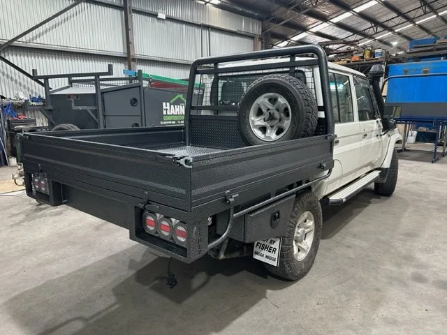 A white ute with a flatbed parked inside a workshop or garage, with a spare tire mounted on the back of the cab. Custom ute tray and powder coating Wagga Wagga. Sandblasting and powder coating service Wagga with custom truck and ute bodies a