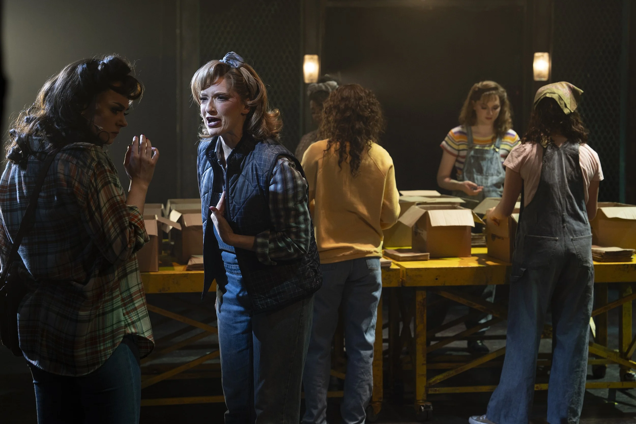 Women having a serious conversation behind a table with boxes on a dimley lit stage