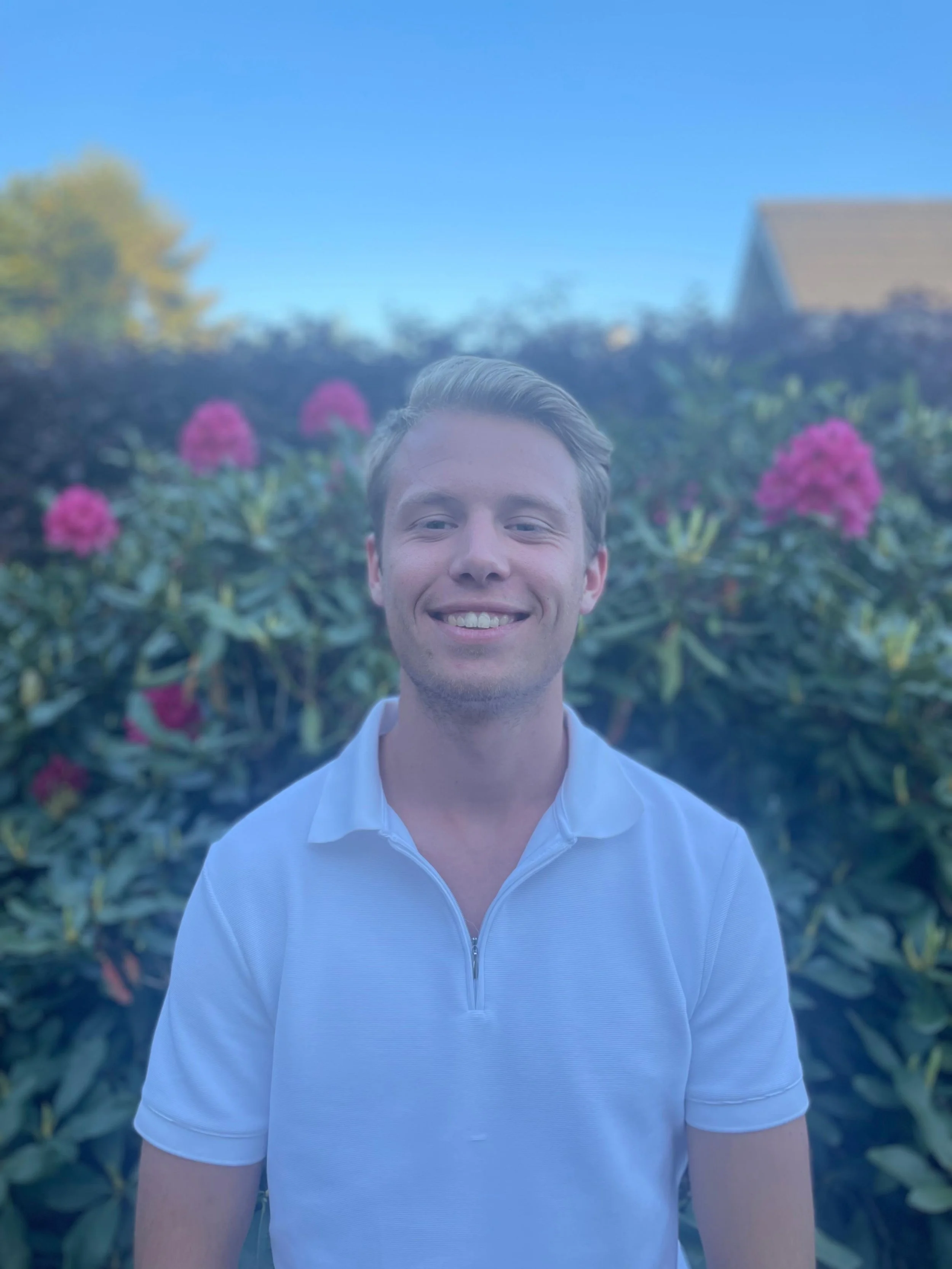 Man in witte polo met achtergrond van bloemen en helderblauwe lucht.