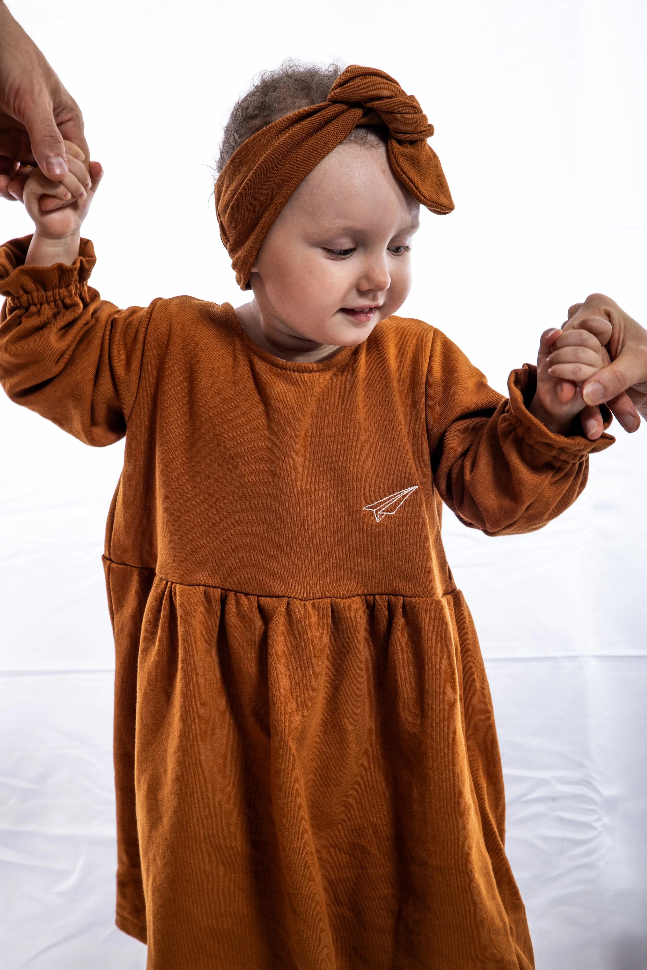 Bambina di tre anni in vestito arancione che tiene per mano i genitori camminando con consapevolezza