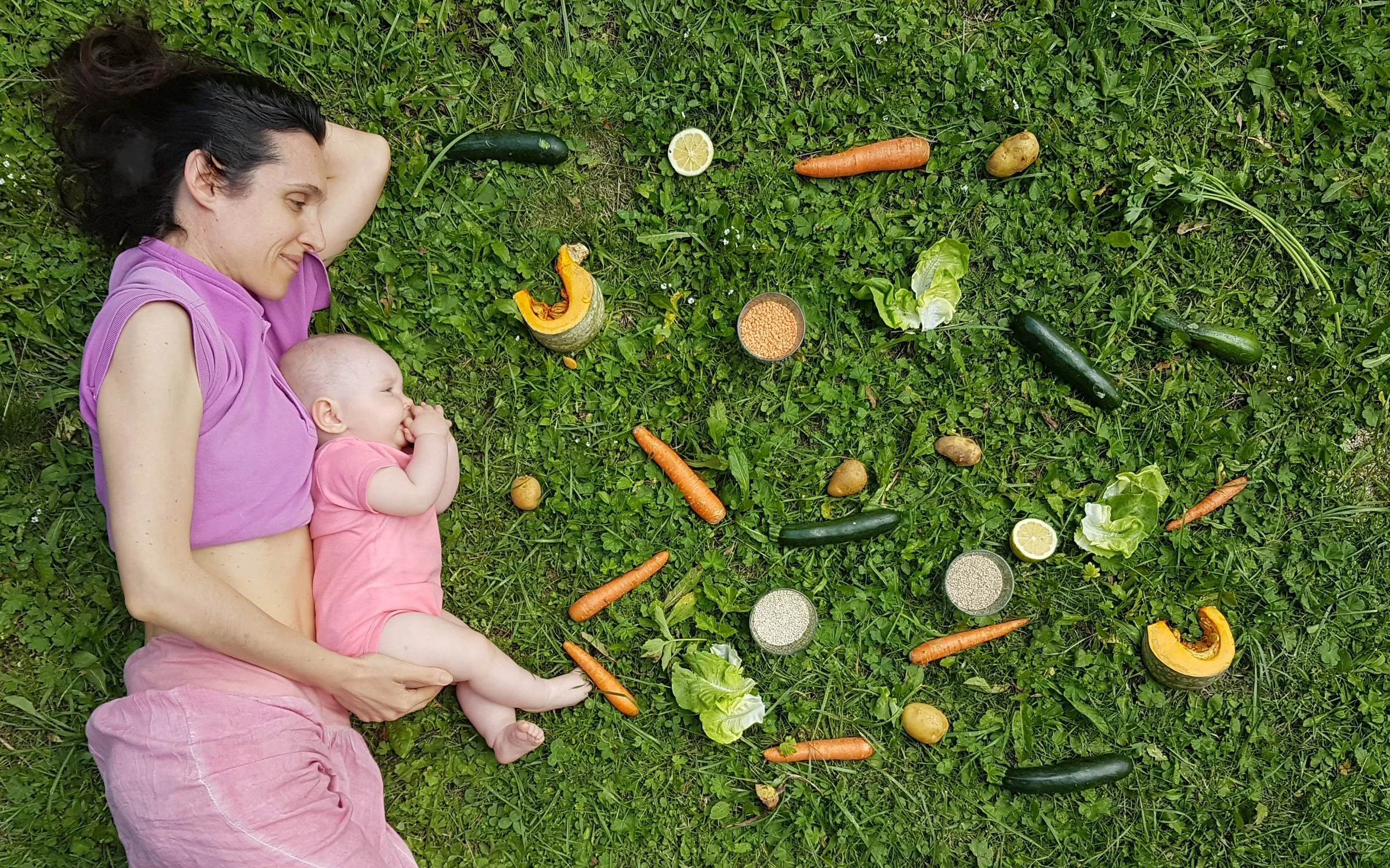 Madre e neonata sdraiate sul prato con cereali e verdura per l'alimentazione vegana e naturale dei bambini