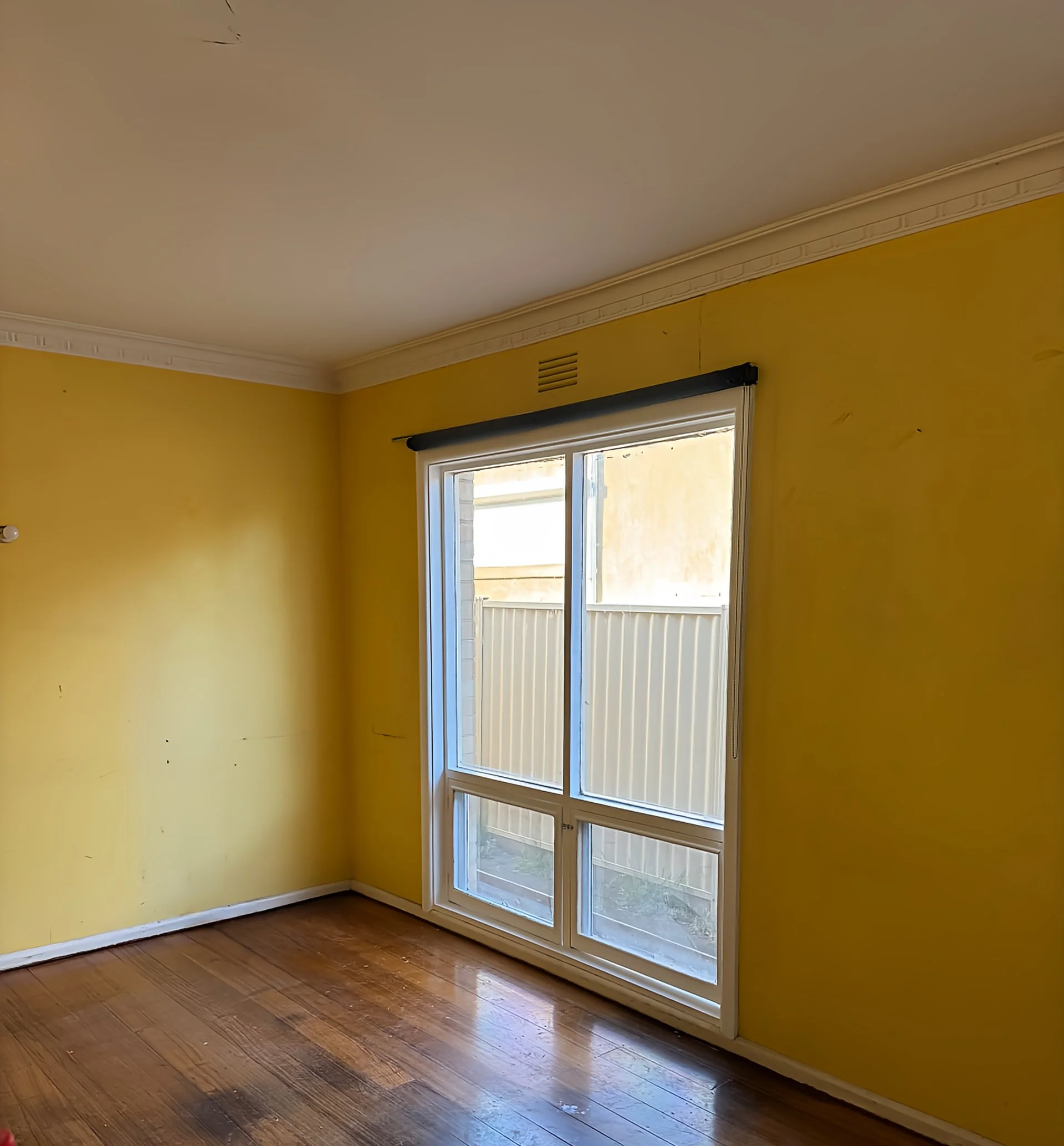 Empty room with yellow walls, hardwood floor, and window with a gray roller blind.