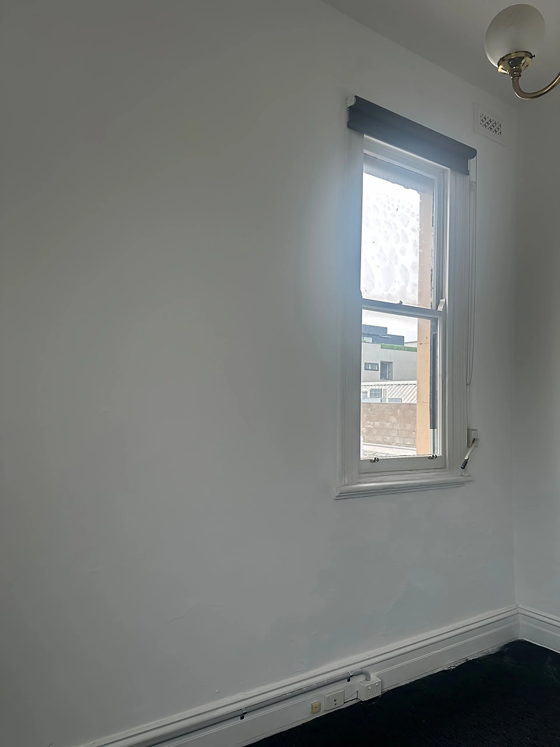 Empty room with white walls, a window with a blue blind, and a ceiling light fixture.