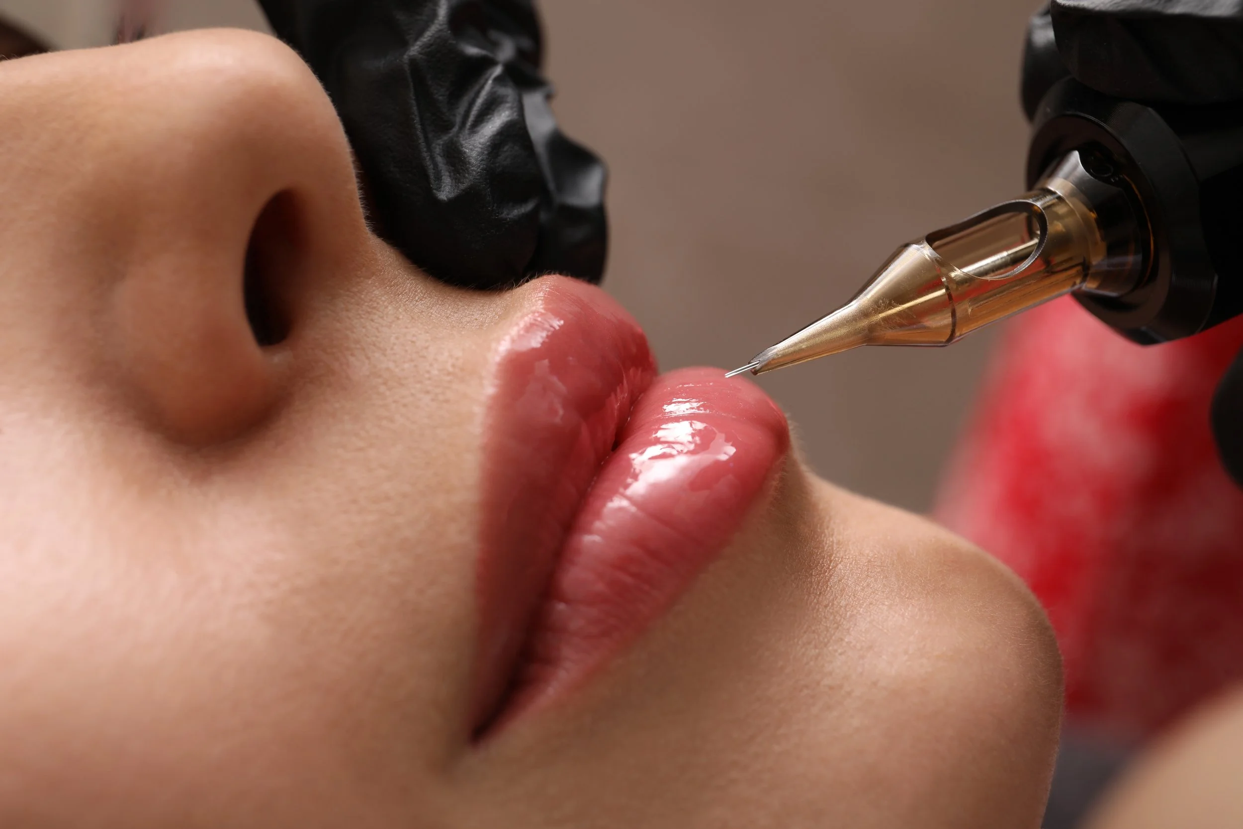 Primo piano di labbra durante una procedura di trucco permanente con un dispositivo per tatuaggi.