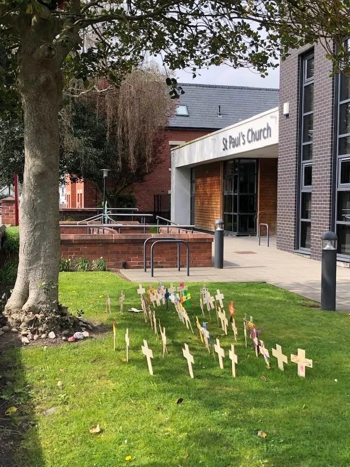 Multiple small crosses planted in the grass outside a church building with a sign reading 'St. Paul's Church'.