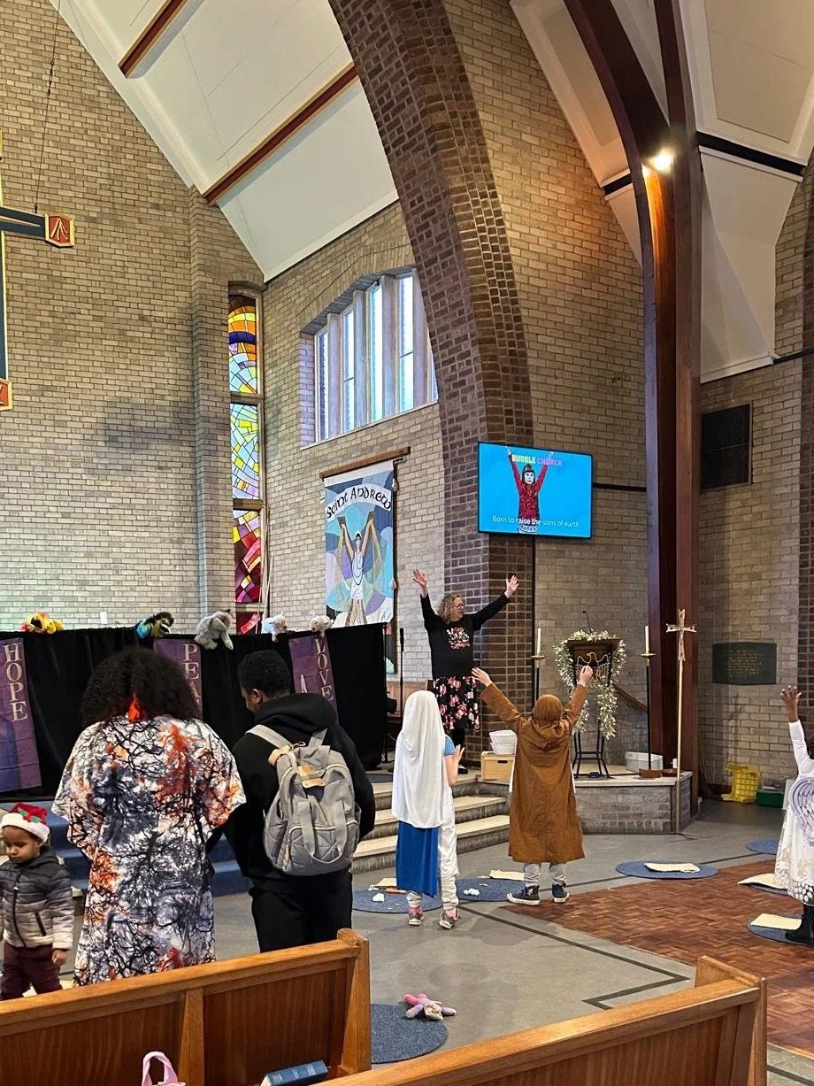 Kids and adults participating in a puppet show inside a church with stained glass windows, a large cross, and a stage platform.