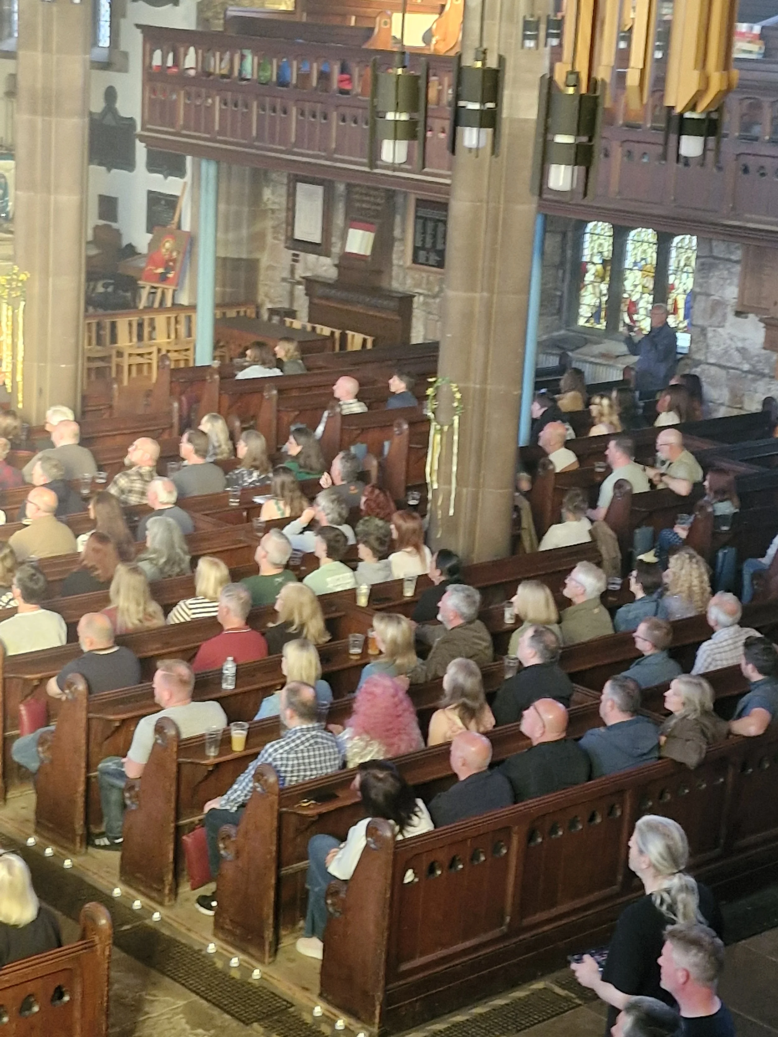 A large group of people seated inside St Elphin's Church, listening to a speaker near stained glass windows, with wooden pews and Gothic architecture.
