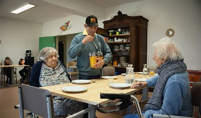 Madeleine, 93 ans, et Jeanne, 94 ans, sont attablées, pendant que Martial, 77 ans, dresse le couvert. Les résidents participent à la préparation des repas • JUSTINE BONNERY