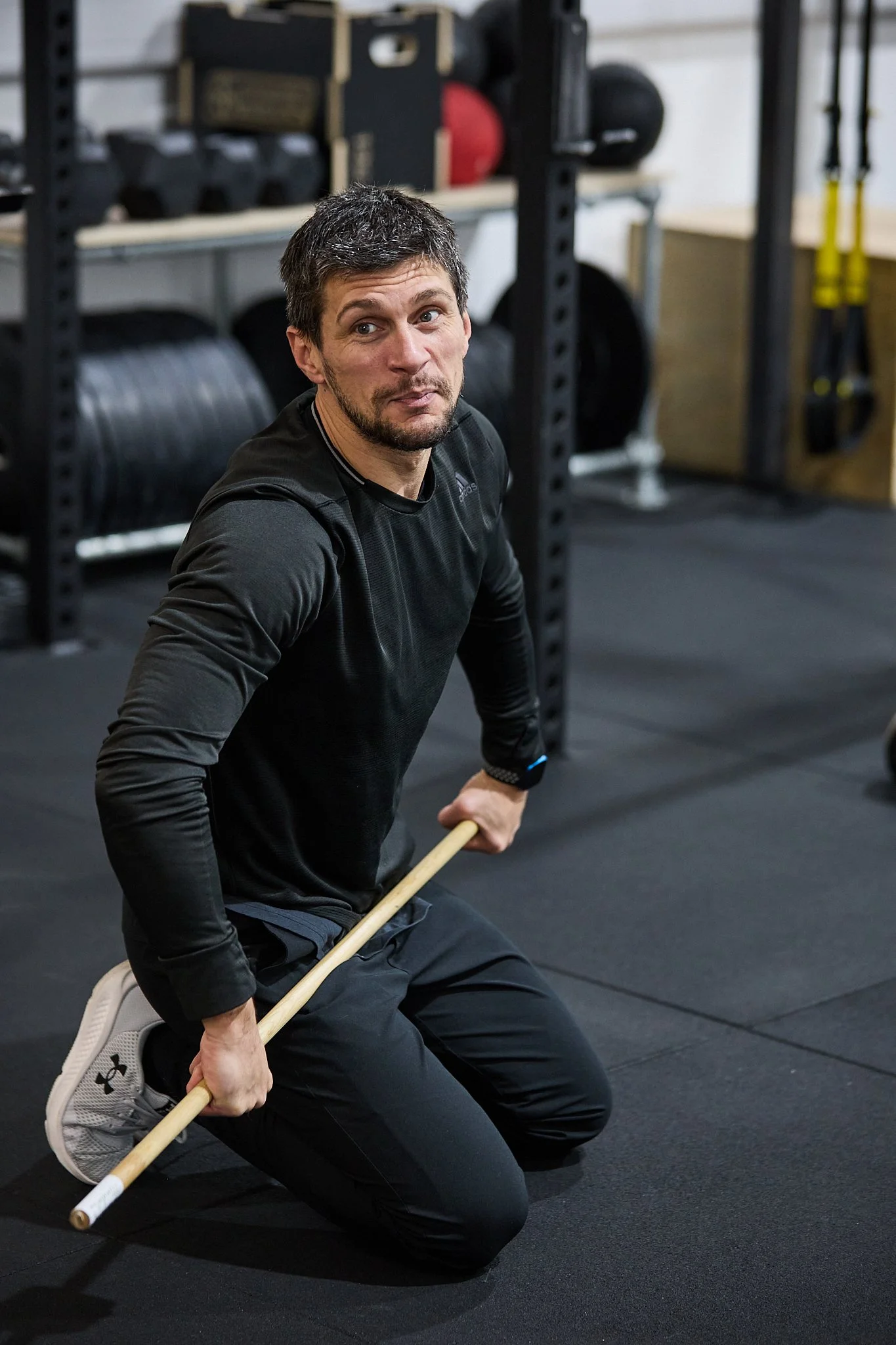 Strength and conditioning coach Silviu Sandu kneeling on the floor holding a wooden pole