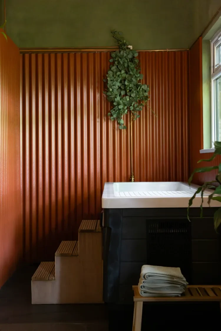 A private cold plunge pool in Contrast Anerley, South London, above wooden steps, and below green plants, beside a window.