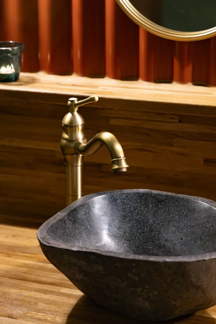 A black stone sink with a brass faucet on a wooden countertop in Contrast Anerley sauna.
