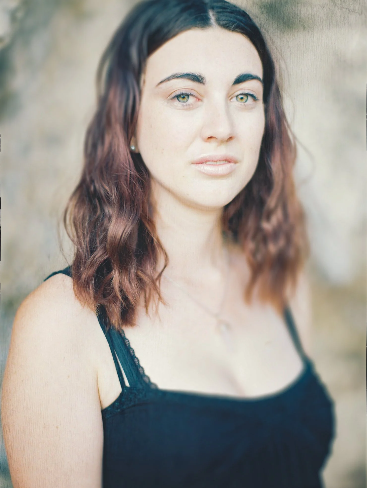 A woman with wavy brown hair and light skin wearing a black top with lace straps, standing outdoors.