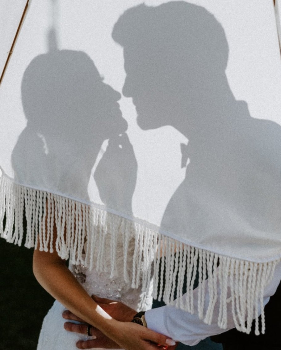 A shadow of a couple in a romantic pose projected on a white fringed fabric, with part of a person's arm and hand visible in the foreground.