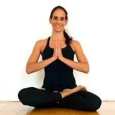 Mulher fazendo yoga em posição de meditação, sentada com as pernas cruzadas e mãos juntas em posição de oração.