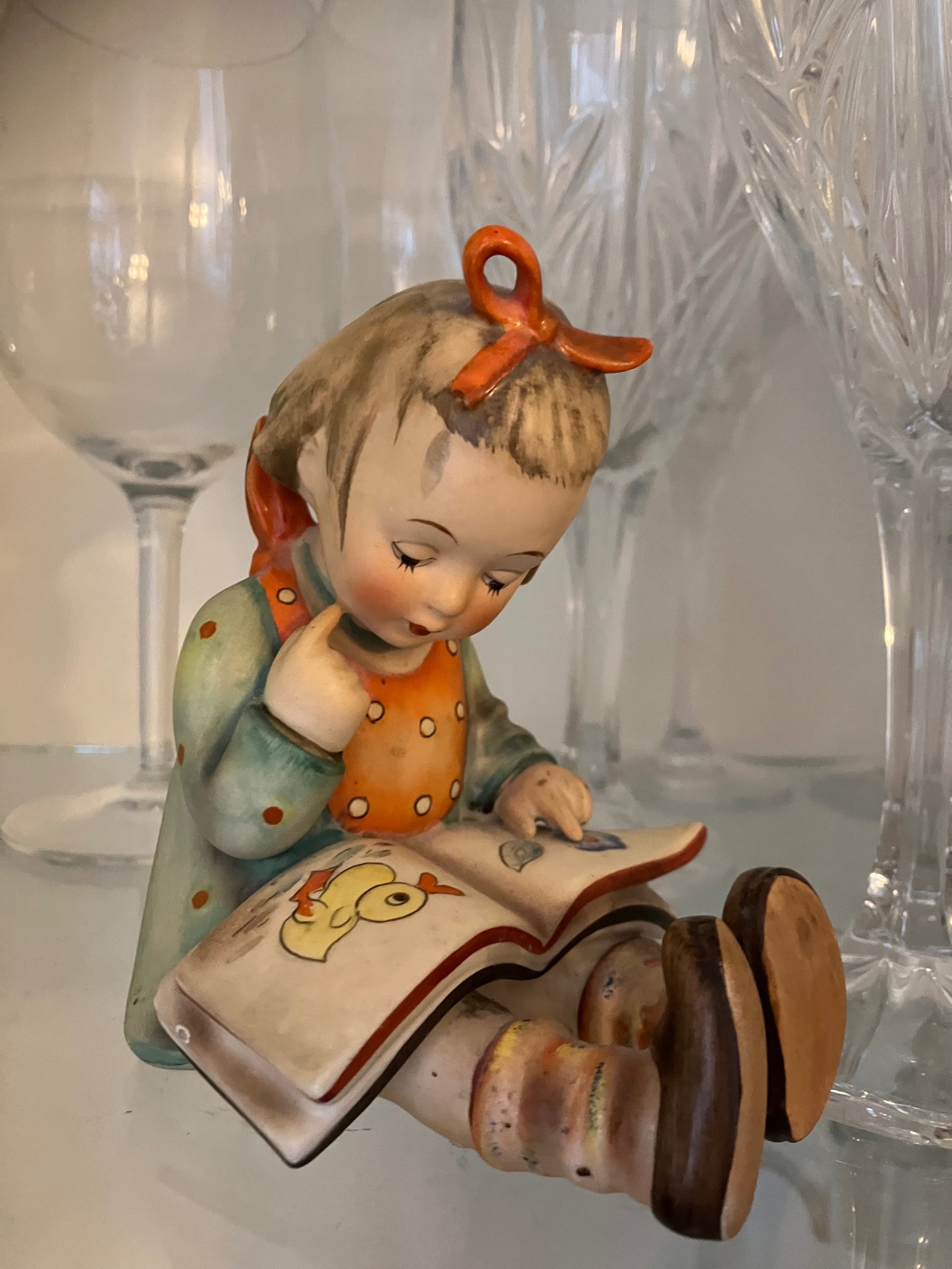 Hummel figurine of a young girl with short hair, tied in a bow, reading a book.