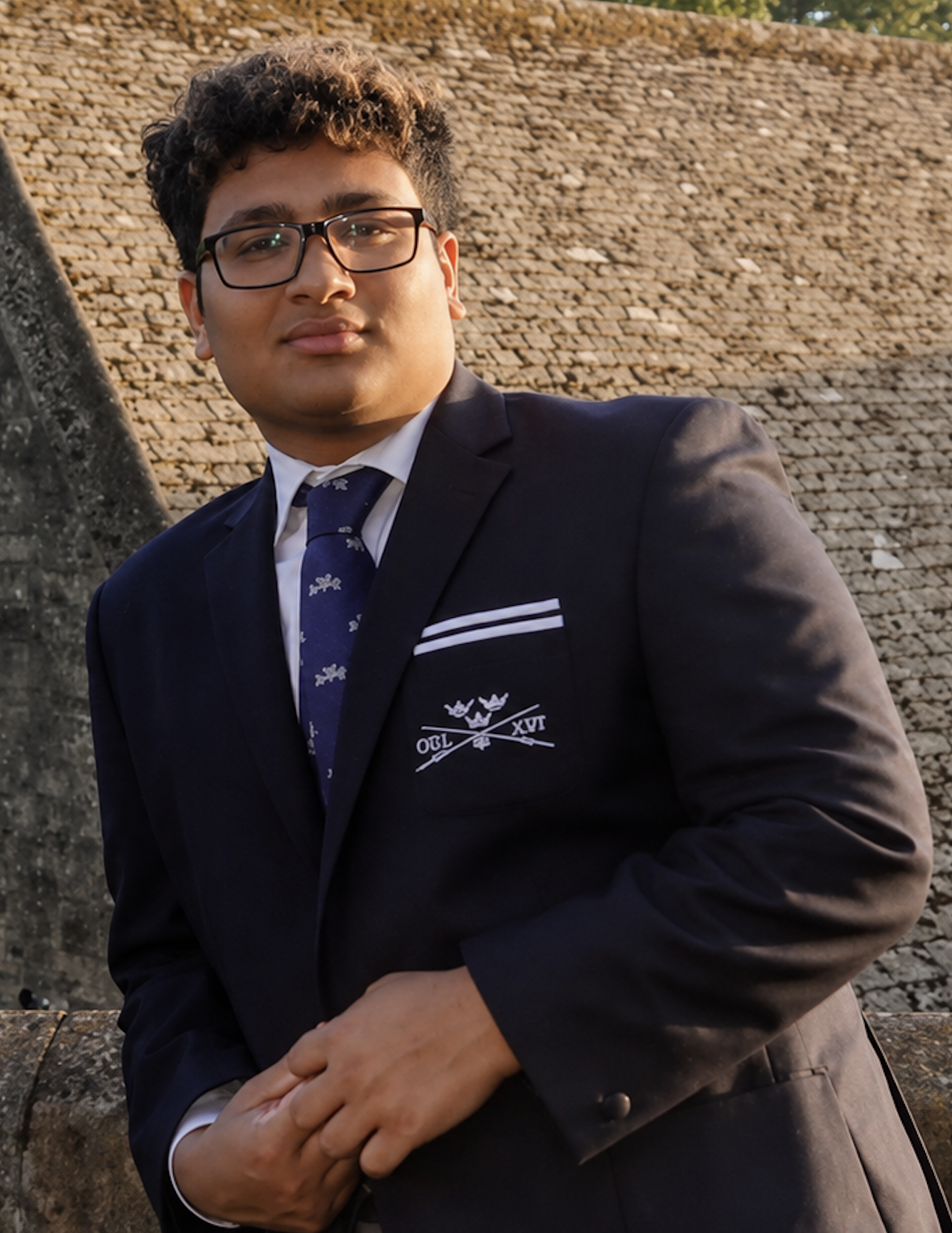 Young man wearing a black tuxedo with a bow tie, standing against a light-colored wall.