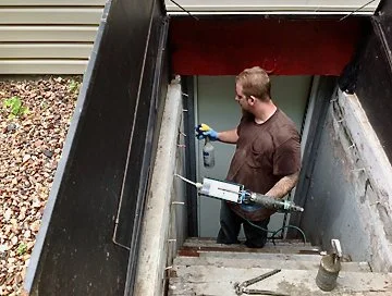 Person applying spray insulation in basement stairwell