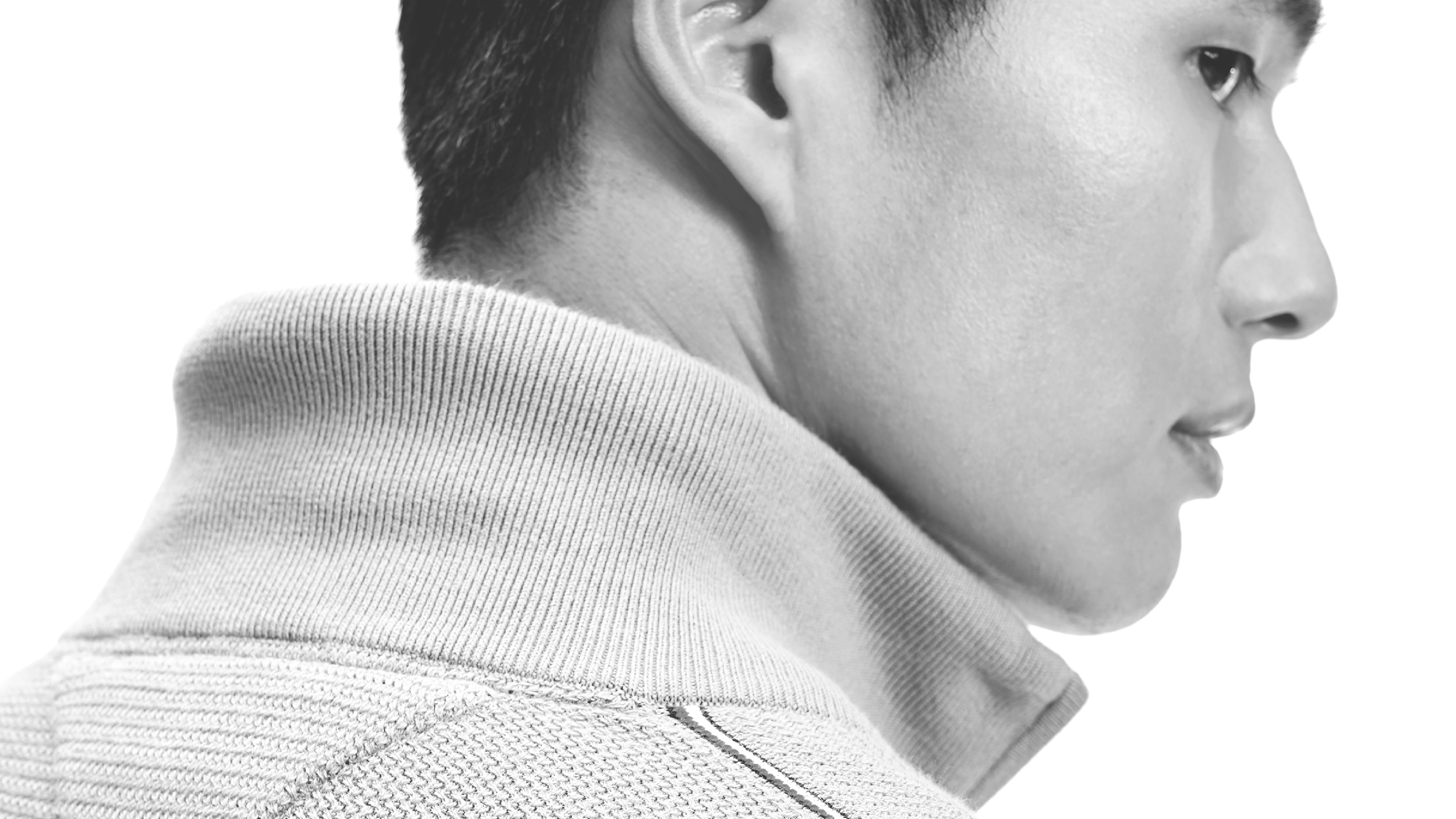 Close-up black and white profile of a young person's face, wearing a textured zipped mock neck sweater.