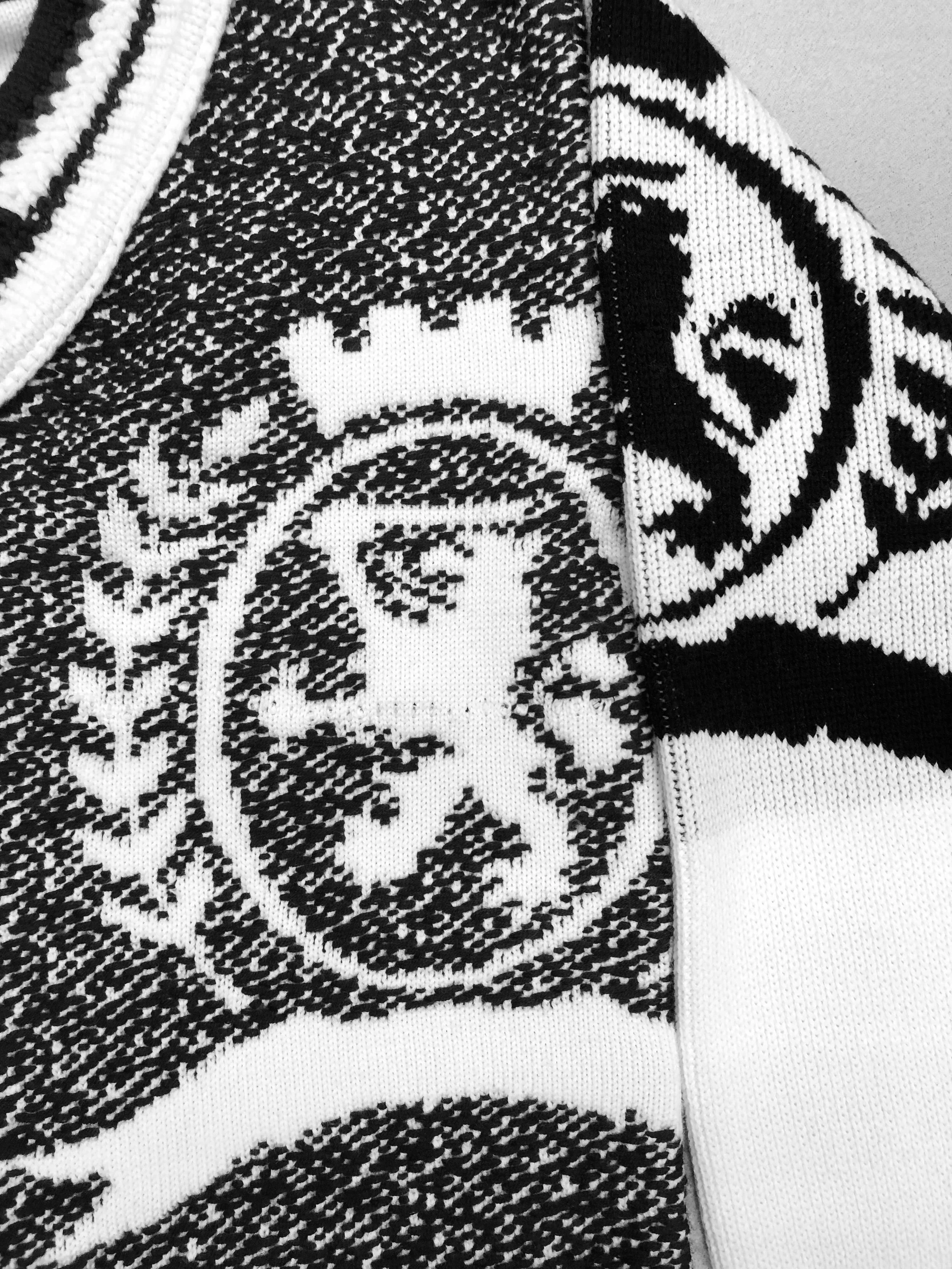 Close-up of a knitted sweater featuring branding graphics, with black and white patterns and clothing.