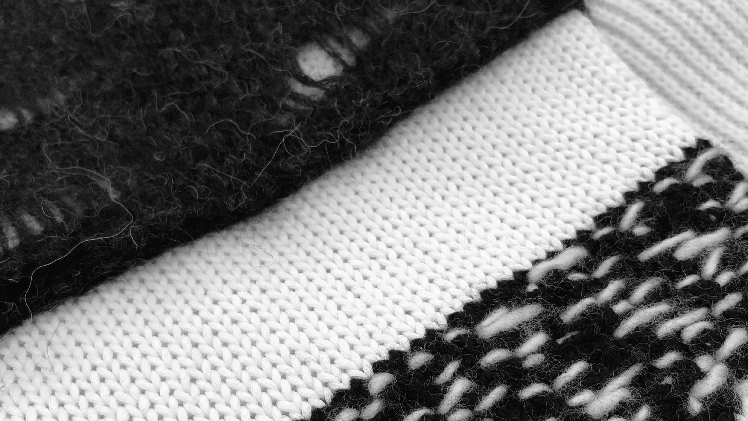 Close-up view of overlapping black, white, and black-and-white knitted sleeve showing different textures and patterns.