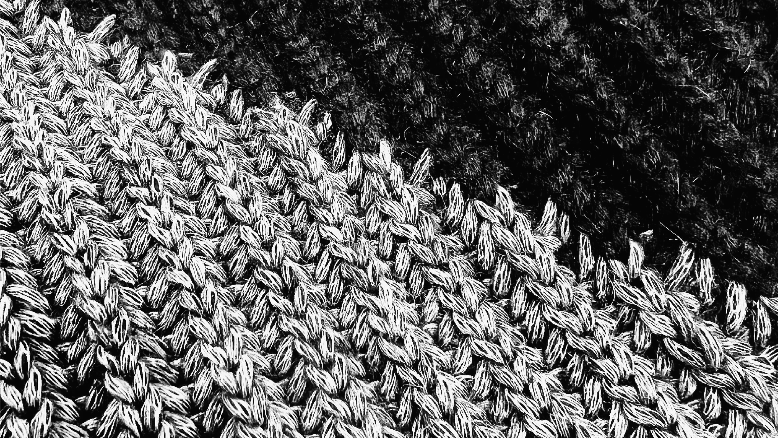 Close-up of a knitted fabric with a chunky knit intarsia, interwoven yarns, showing textures of light and dark yarn sections.