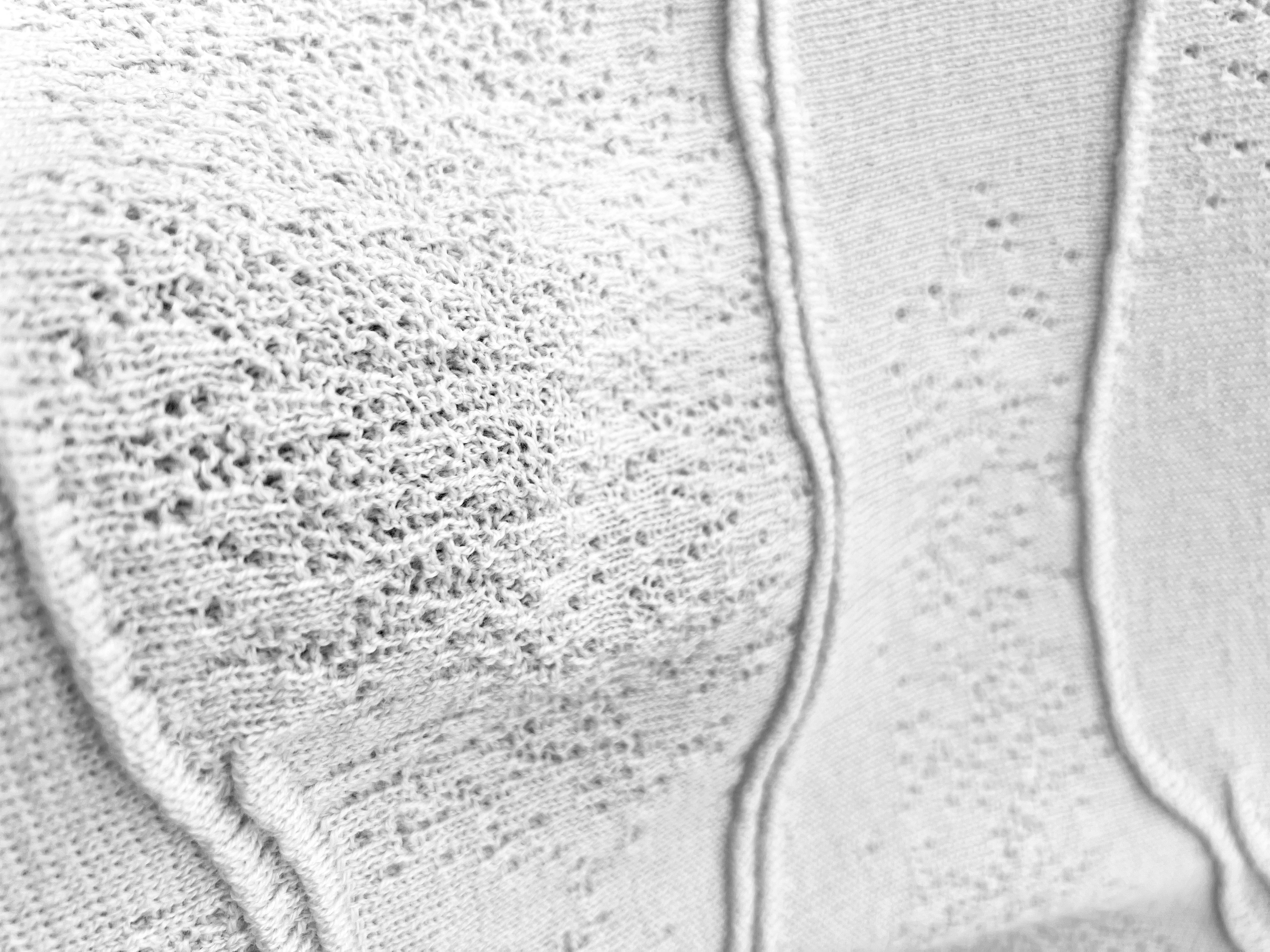 Close-up of a light-colored textured irregular lace knit with ottoman lines and goring knitting techniques. 