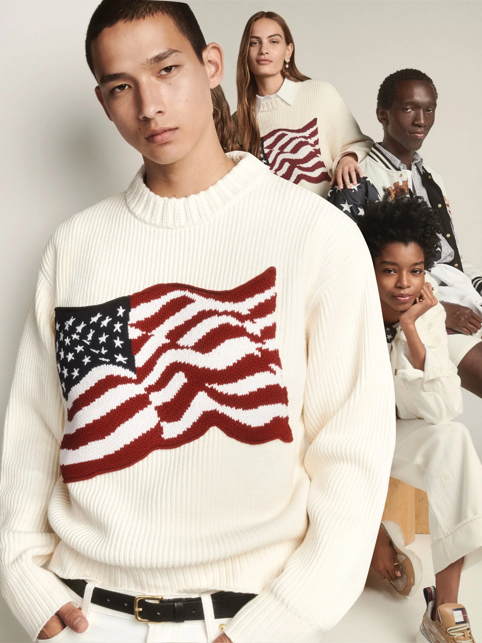Four diverse models, including males and females of different ethnicities, wearing sweaters with American flag designs, posing against a plain background in a fashion photoshoot.